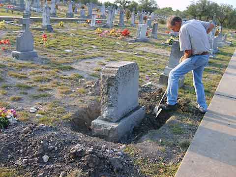 Digging around the base to secure resetting a headstone Working to clean and reset headstone